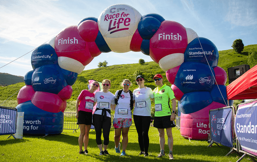 A group of five participants from the company Standard Life, posing for a photo at the Race for Life finish line.